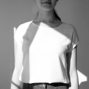 Black and white photo of a woman in a white t-shirt, with sunlight casting shadows.
